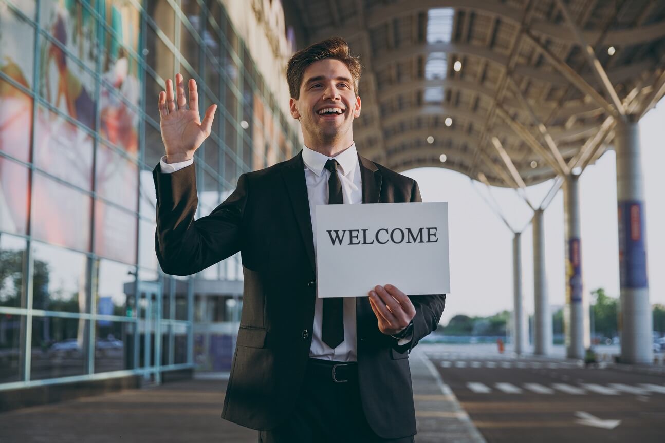 Professional SuperShuttle driver smiling and waving with a Welcome sign at the airport